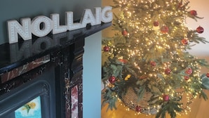 A fireplace with a sign that reads 'NOLLAIG' and a decorated Christmas tree with lights and ornaments.