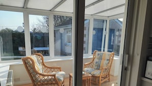 A conservatory with wicker furniture, a glass table, and a view of the outside.