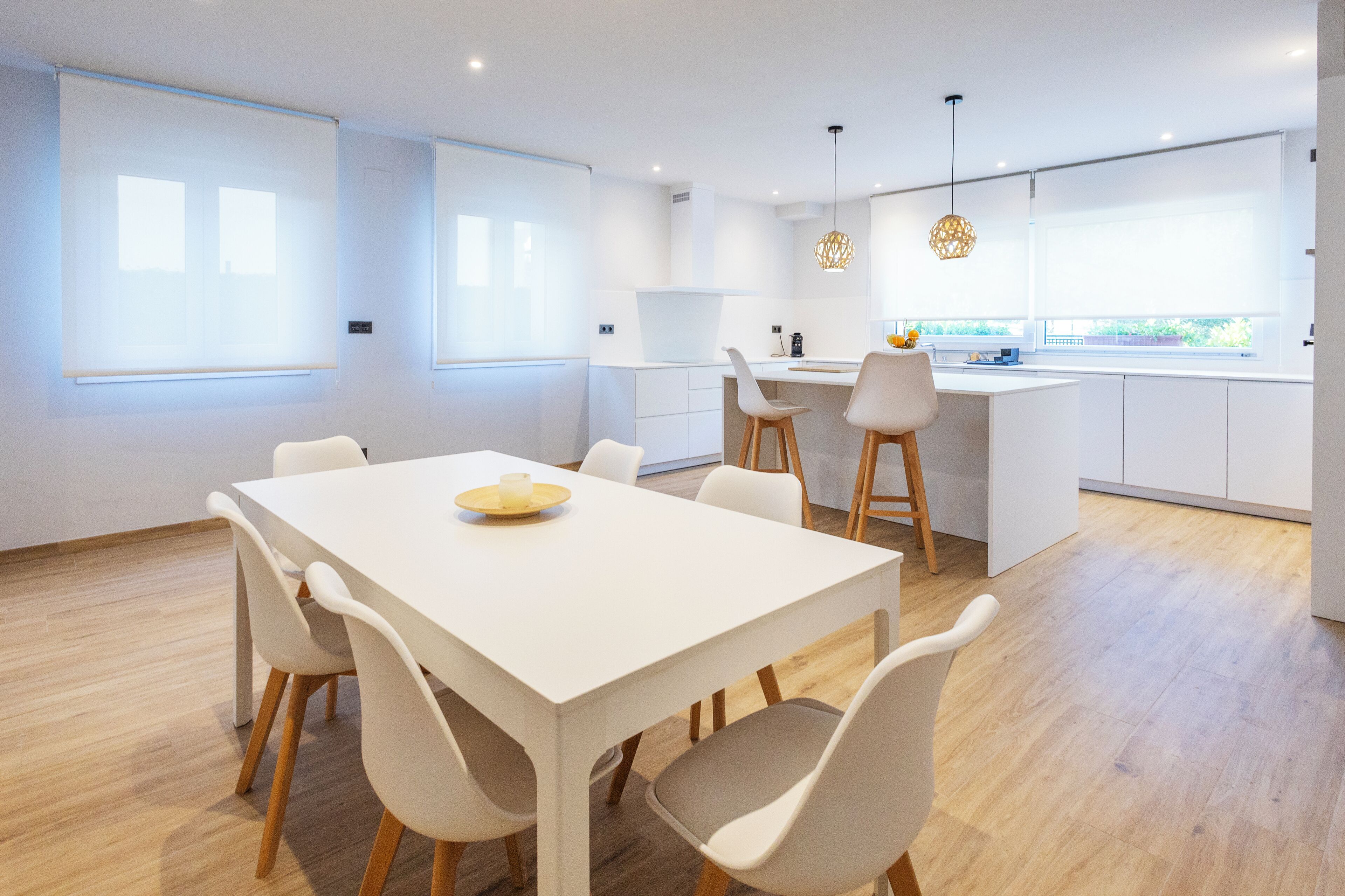 Una cocina moderna con encimera blanca, sillas de madera e iluminación colgante.