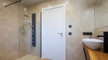 Un baño moderno con cabina de ducha de vidrio, una puerta blanca y un tocador de madera con lavamanos.