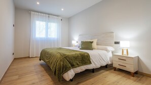 A bedroom with a bed, bedside tables, a window with curtains, and a wooden floor. - Bizi Baztan Goienetxea (Elizondo)
