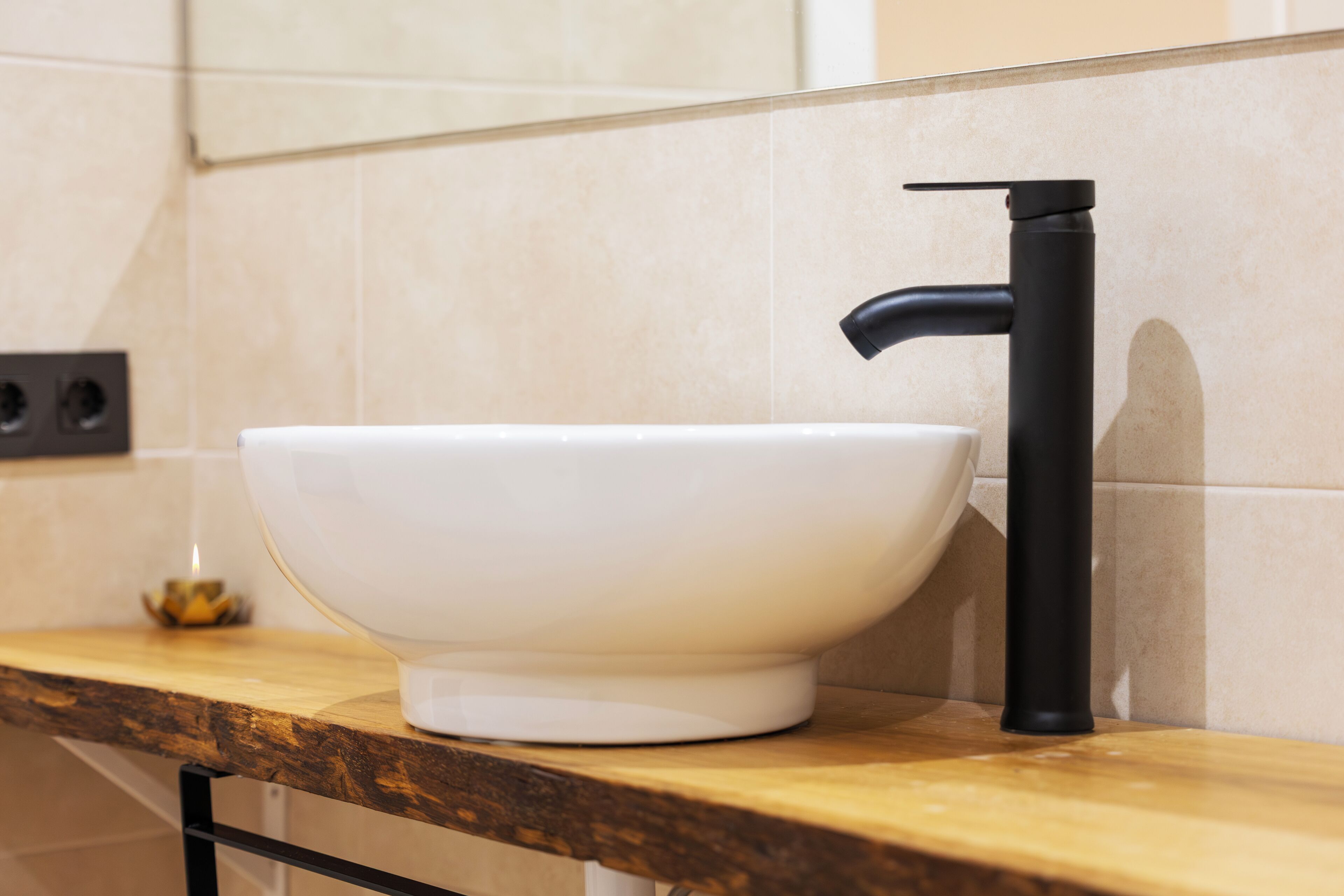 A bathroom with a white basin, black faucet, and wooden countertop.