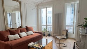 A living room with a red sofa, a blue ottoman, a glass coffee table, and a large mirror. - Spacious, Quiet and Elegant Apartment in Paris (Paris)