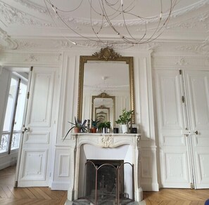 Une pièce dotée d’une cheminée blanche, d’un grand miroir et d’un plafond orné de motifs complexes.