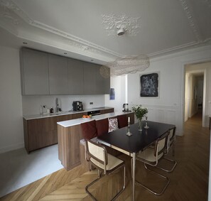 A modern kitchen with a central island, wooden cabinets, and a dining area with a table and chairs. - Spacious, Quiet and Elegant Apartment in Paris (Paris)