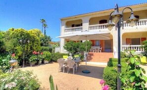 Un immeuble de deux étages doté d’un balcon, d’un espace extérieur aménagé pour s’asseoir et d’un jardin.