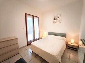 Une chambre à coucher comprenant un lit, des tables de chevet, une commode, une fenêtre avec des rideaux et une œuvre d’art accrochée au mur.