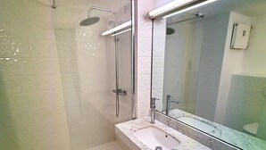 Une salle de bain dotée d’une douche à parois de verre, d’un lavabo avec un plan de toilette en marbre et d’un grand miroir.