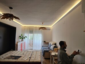 A modern living room with a sofa, a dining table, and a ceiling fan. - Apartment Near the Beach in El Bajoncillo (Torremolinos)