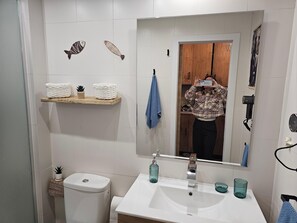 A bathroom with a white sink, two glass cups, a mirror, and a shelf with towels and a small plant. - Apartment Near the Beach in El Bajoncillo (Torremolinos)