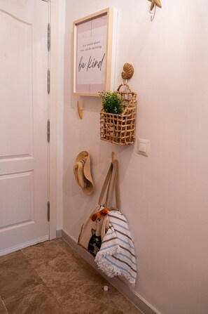 A hallway with a white door, a framed inspirational quote, a woven basket with a plant, a pair of sandals, and a striped towel. - Apartment Near the Beach in El Bajoncillo (Torremolinos)