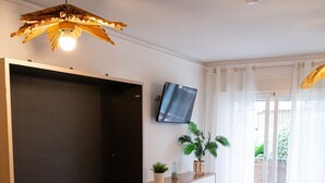 Makuuhuoneessa on sänky, televisio, kattotuuletin, huonekasvi ja liukuovet, jotka ovat lasia.