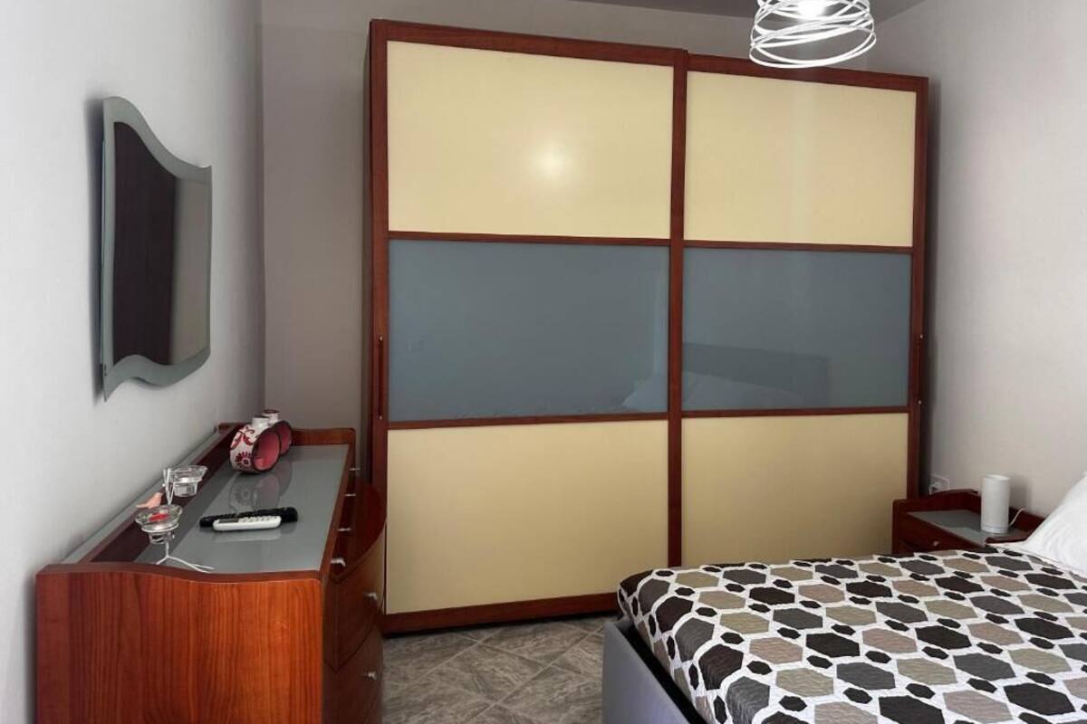 A bedroom with a bed, a dresser, a mirror, a wardrobe, and a hanging light fixture.