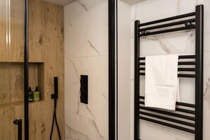 Ein modernes Badezimmer mit Waschtisch aus Holz, Marmorwänden, einem schwarzen Handtuchhalter und einer Duschkabine.