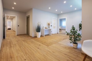 A spacious hallway with wooden flooring, white walls, and a central white console table with plants.
