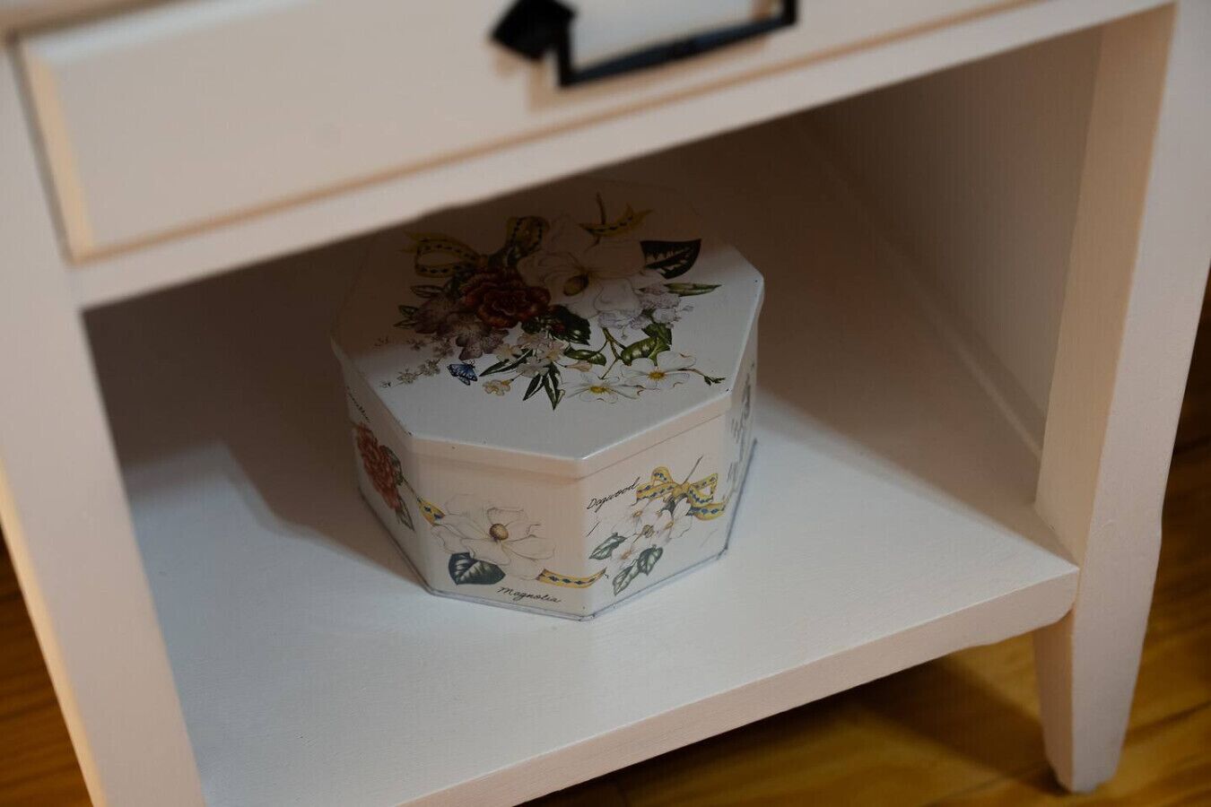 Een witte opbergdoos met bloemmotieven op een witte plank.