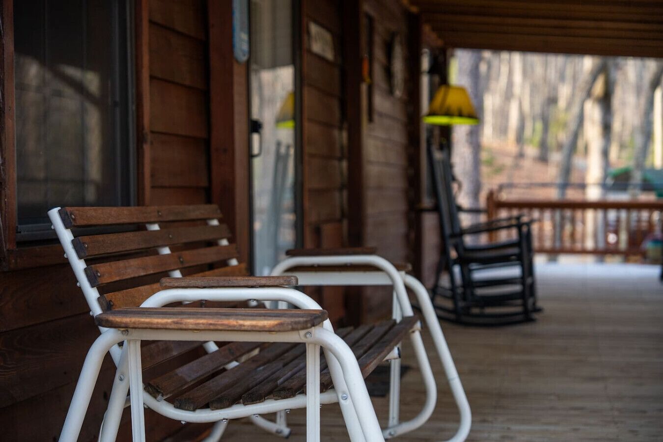 A wooden porch with two metal chairs and a bench.