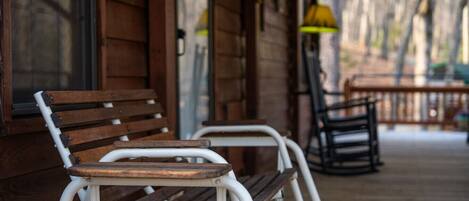 A wooden porch with two metal chairs and a bench.