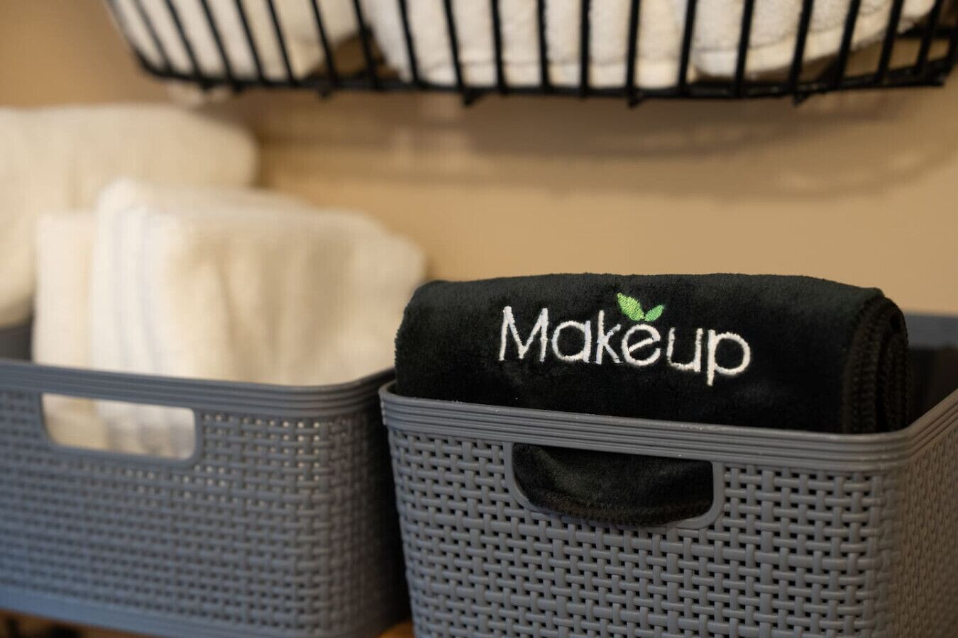 A storage bin labeled 'Makeup' with a black cloth inside, placed next to a white cloth in a basket.