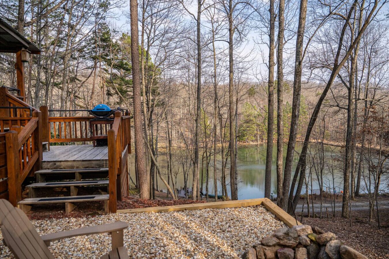 A wooden deck with a bench and a kayak, overlooking a lake surrounded by trees.