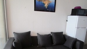 Ein dunkelbraunes Sofa mit drei Kissen, ein weißer Kühlschrank und ein gerahmtes Bild an der Wand.