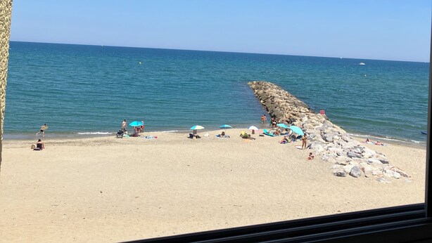 Blick auf einen Strand durch ein Fenster, strahlend blauer Himmel, Sand und das Meer.
