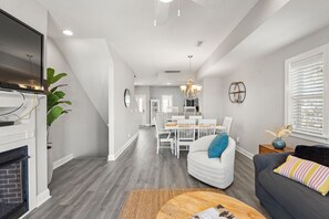 Ein modernes Wohnzimmer mit Kamin, Essbereich und einer Treppe, die zu einer oberen Ebene führt.