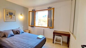 Een slaapkamer met een bed, nachtkastjes, een raam met gordijnen, een wandlamp en een lijst met een afbeelding.