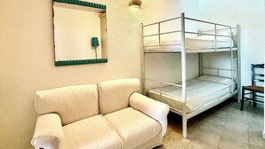 Ein Stockbett, eine Schlafcouch und ein wandmontierter Spiegel in einem Zimmer mit Fliesenboden.