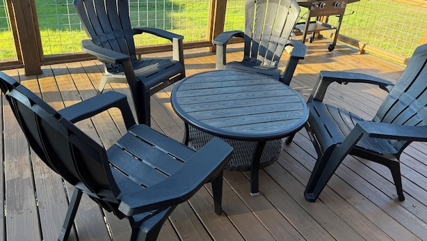 A deck with a round table and four Adirondack chairs, a grill, and a wooden railing.