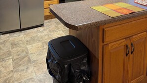 A kitchen with wooden cabinets, a stainless steel refrigerator, a microwave, a stove, and a trash can.
