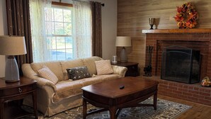 A living room with a sofa, coffee table, fireplace, and a ceiling light fixture.