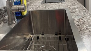 En diskho i rostfritt stål med ett modernt blandare, en bänkskiva i granit och en inbyggd spis.