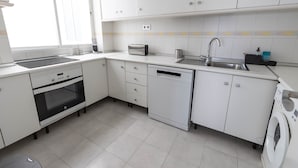 A modern kitchen with white cabinets, a built-in oven, a dishwasher, and a washing machine. - Beachfront Vacation Apartment - Almunecar (Almunecar)