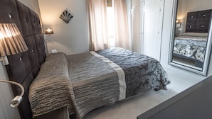 A bedroom with a bed, a headboard, a bedside lamp, a mirror, and a window with curtains. - Beachfront Vacation Apartment - Almunecar (Almunecar)