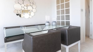 A dining area with a glass-top table, wicker chairs, and a wall-mounted mirror. - Beachfront Vacation Apartment - Almunecar (Almunecar)