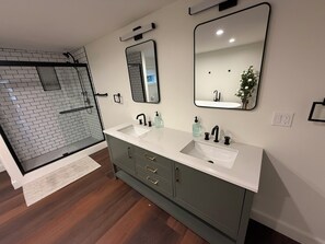 A bathroom with a shower, two sinks, a vanity, and two mirrors. - Beautiful 4BR Lake House - New 2026 - Boat Slip - Located on Large Compound (Laconia)