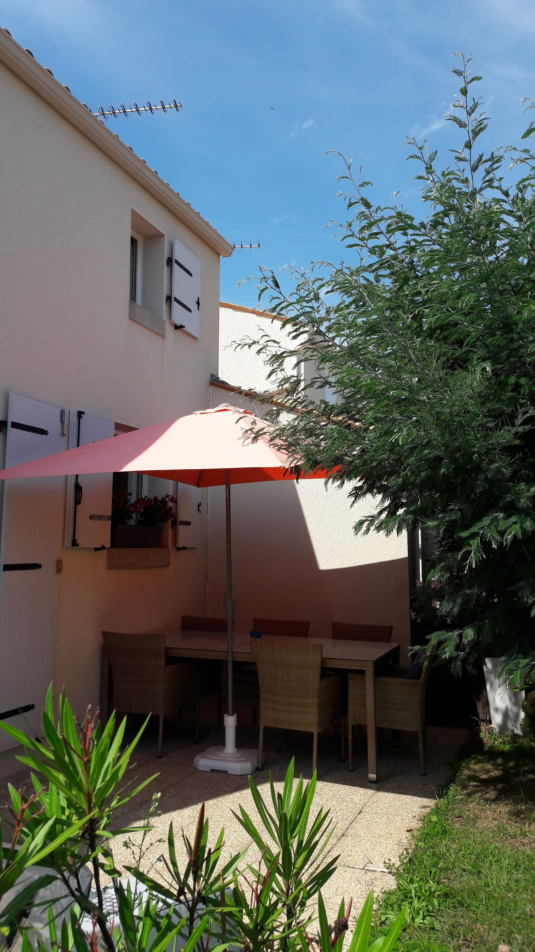 A patio area with a table and chairs, a red umbrella, and a building with a white exterior.