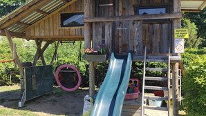 A rustic wooden playhouse with a slide, surrounded by greenery.