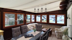 A dining area with a table, chairs, and a view through large windows.