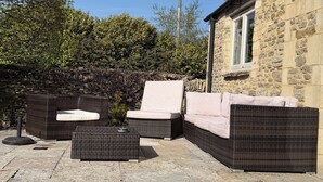 A patio with wicker furniture, a stone wall, and a building with a window. - Luxury Cotswold Cottage Can Sleep 8. Secure Garden & Parking.  Walks From Door (Poulton)