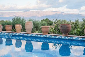 Une piscine bordée de pots en terre cuite alignés le long du bord, une bordure carrelée et un paysage montagneux en arrière-plan.