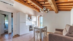 Un'ampia zona giorno con tavolo e sedie da pranzo, un divano, una cucina con pensili bianchi e un soffitto in legno.
