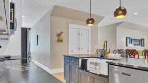 A modern kitchen with a central island, pendant lighting, and a dining area with a red chair.