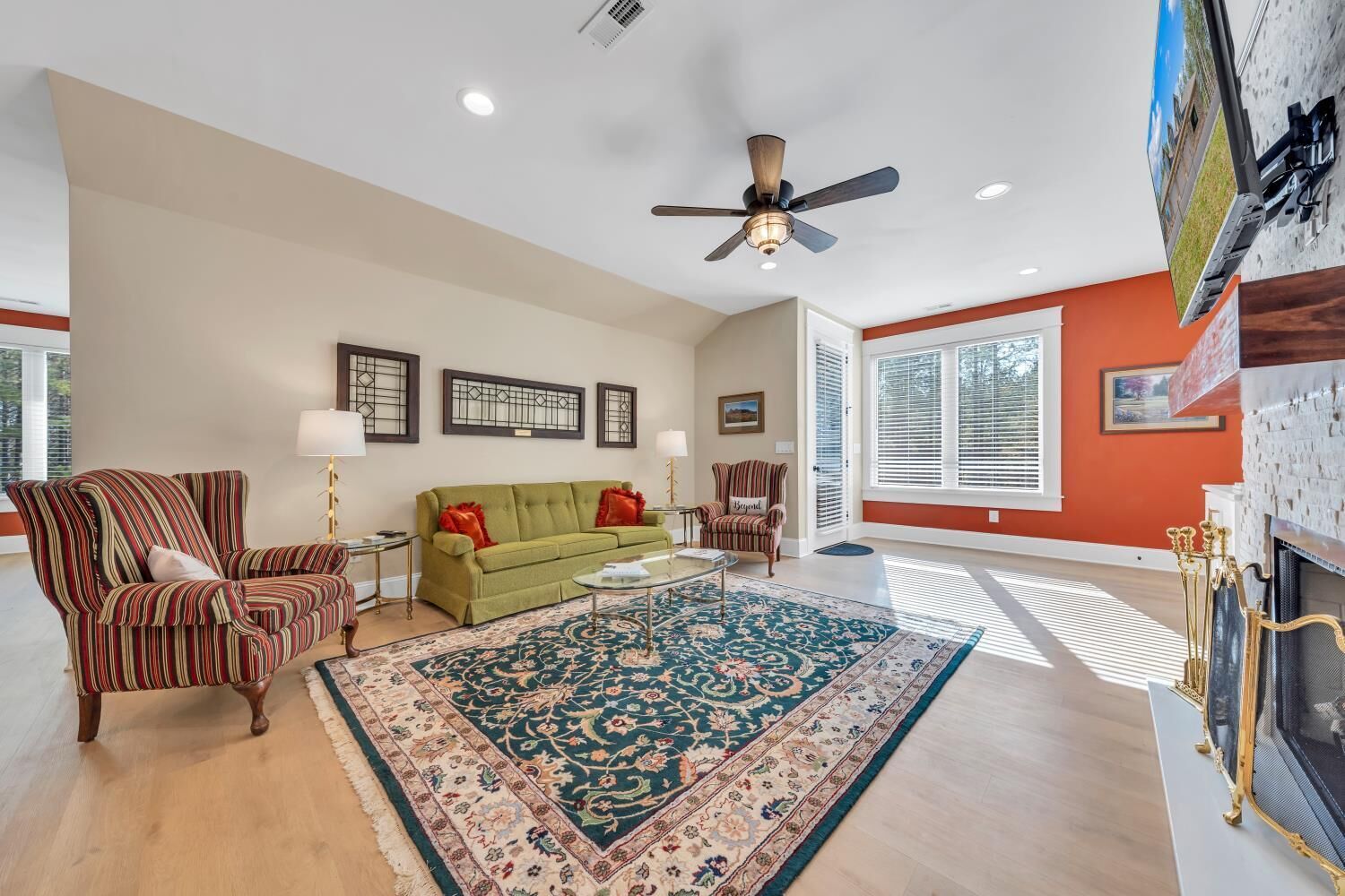 A spacious living room with a green sofa, striped armchairs, a large rug, and a fireplace.