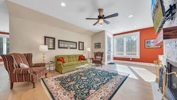 A spacious living room with a green sofa, striped armchairs, a large rug, and a fireplace.