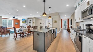 A modern kitchen with a central island, white cabinetry, and a dining area with wooden chairs.