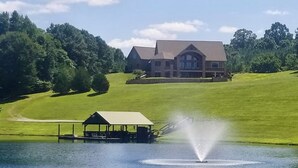 A large house with a dock and a fountain by a lake.