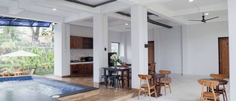 A spacious indoor area with a pool, wooden flooring, and a dining area with chairs and tables.
