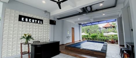 A modern hotel lobby with a reception desk, a large indoor water feature, and a view of the outdoor garden.